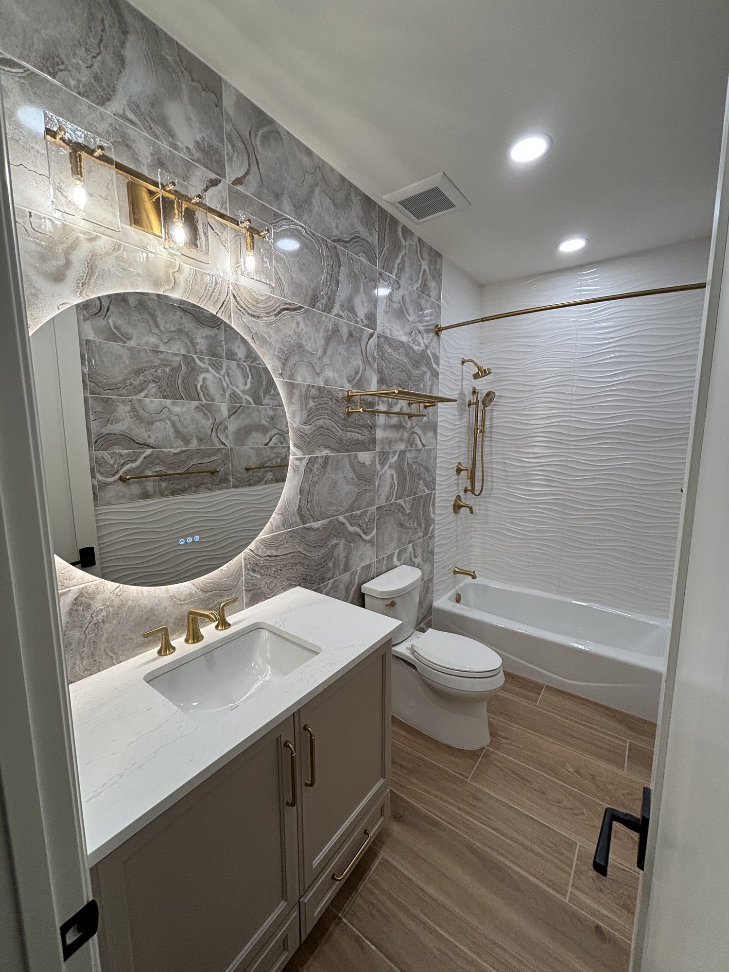 Guest bathroom with backlit round mirror and vanity sconce lighting in Tampa custom home by Dim and Dimmer Electric