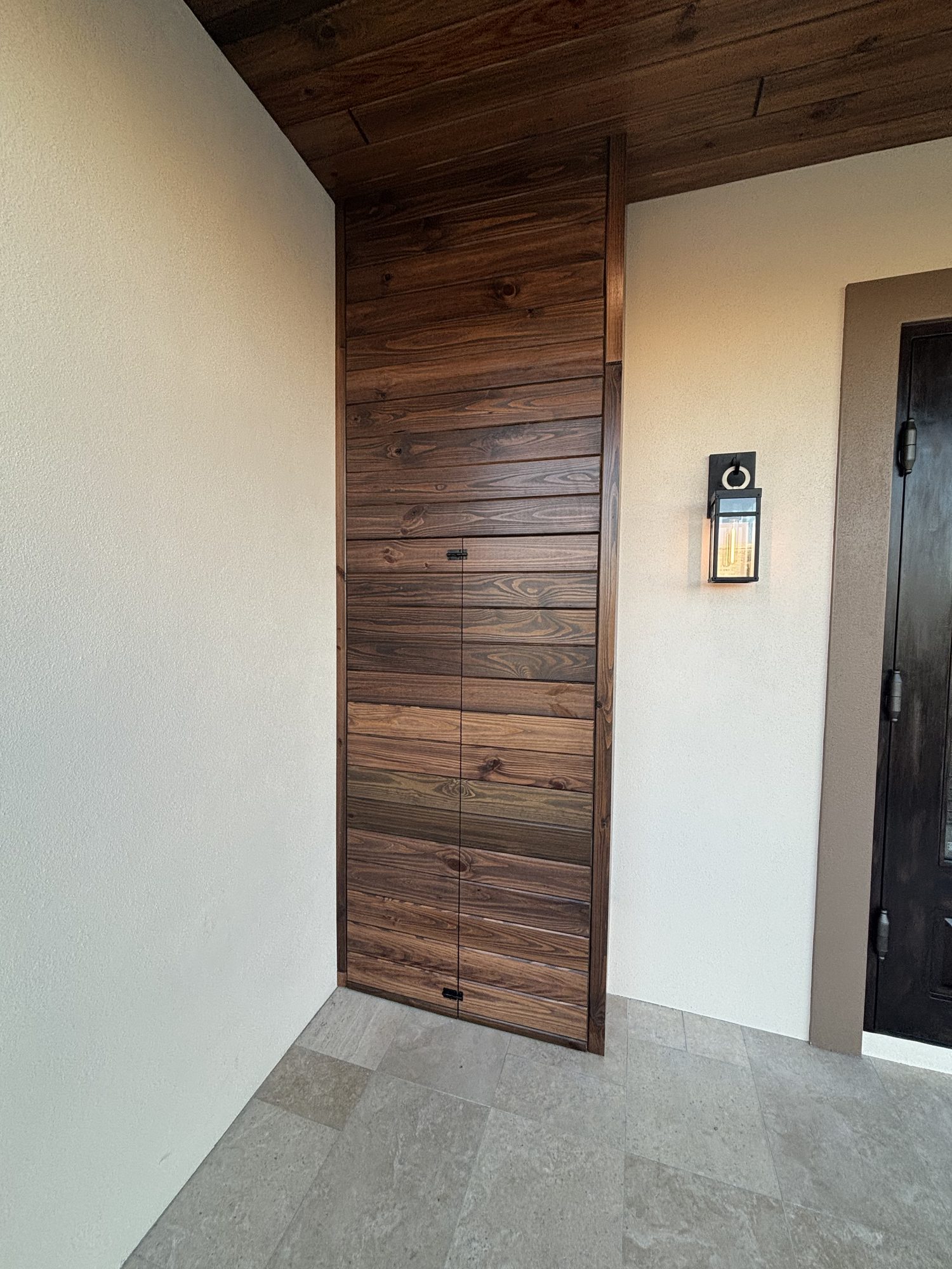 Concealed electrical panel closed flush with wood feature wall beside entry sconce and video doorbell, Tampa custom home by Dim and Dimmer Electric